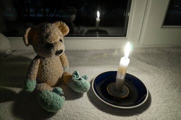 Blackout. A teddy bear sits in the dark on the windowsill near the window next to a burning candle....