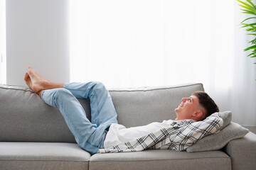 Horizontal photo with copy space of a relaxed man lying on the sofa smiling looking up