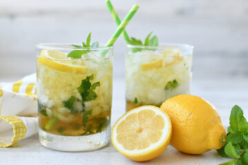 Cocktail or lemonade drink with lemon, muddled mint garnish, green straws, lemon slices