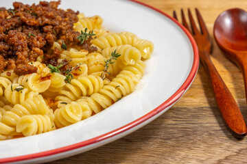 Ground Beef Pasta with fresh thyme on ceramic plate over wooden background.