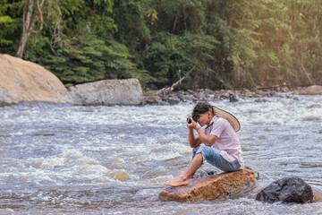 lifestyle. young latino man sitting on a rock taking pictures with an analog camera