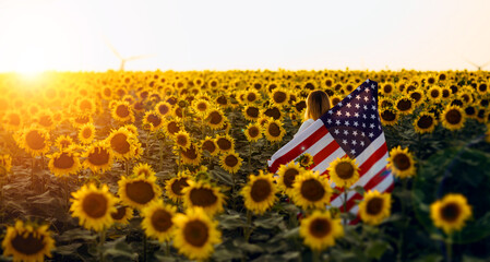 Beautiful young woman with the American flag in a sunflower field at sunset. 4th of July....