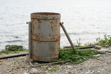 Old rusty, holey urn with traces of metal corrosion on the seashore