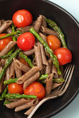 Spring integral buckwheat pasta penne with young asparagus and cherry tomatoes. Italian healthy diet recipes, seasonal spring vegetables. Delicate blue background, close up