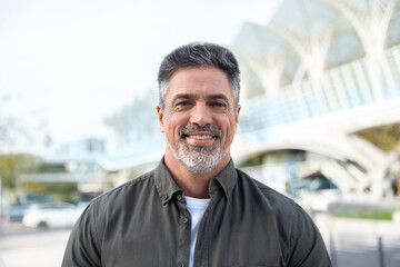 Naklejka premium Lifestyle portrait of European middle age mature adult man. Freelancer entrepreneur standing outdoor at street. Happy handsome 40 years old latin hispanic businessman smiling at camera with sun ray