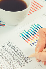 Cup of coffee and finger showing financial chart with production or sales statistics. Business