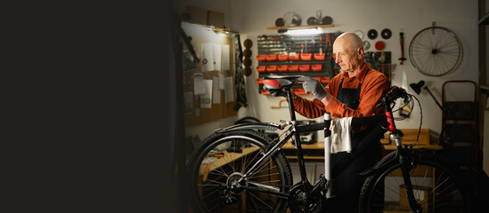 Old male mechanic working in bicycle repair shop, mechanic repairing bike. Copy space
