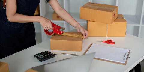 Woman use scotch tape to attach parcel boxes to prepare goods for the process of packaging at home, shipping, online sale internet marketing ecommerce concept startup business idea