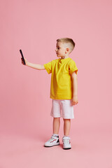 Child, preschooler holds phone and talking with parents on videocall against pink studio background. Virtual lesson class. Concept of fashion and style, beauty, back to school, e-learning. Ad