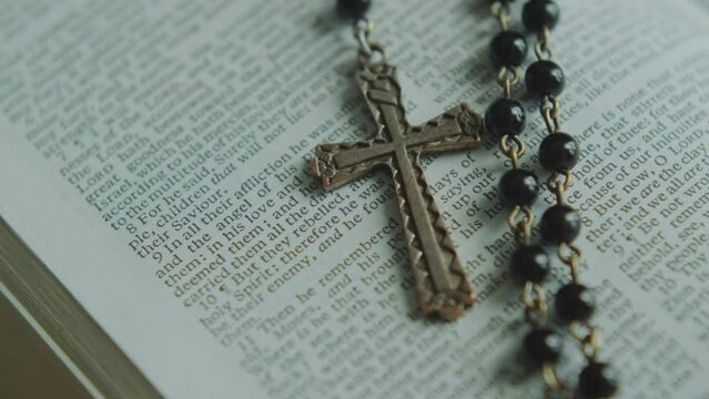 Page of opened Bible with religious text and rosary beads with crucifix pendant on it. Extreme close-up view