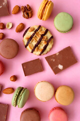 Pastel macarons, almond chocolate, peanut butter cookies and various nuts on bright pink background. Top view.