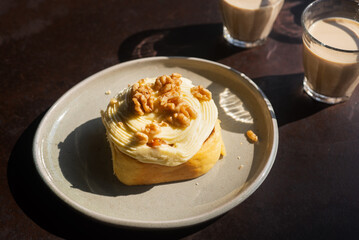 Homemade mixed fruit cinnamon roll with cream cheese frosting and walnuts on top on a ceramic plate