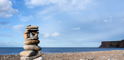 Stack of zen stones with by the sea blurry blue sky backgroud, Close up Balancing of pebble rocks stacked on top of each other on the sand beach.Zen like concepts.