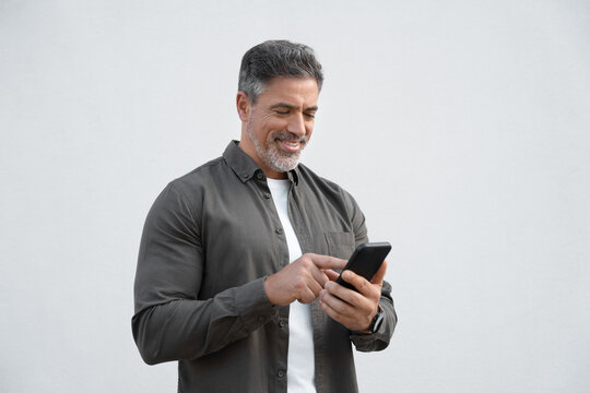 Smiling hispanic business man using smartphone mobile phone device for online financial bank transactions. 40s freelancer entrepreneur in casual shirt holding cellphone isolated on white background