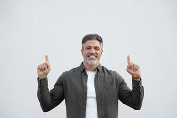 Smiling mature 40s old grey haired businessman in casual clothes, pointing up above head both hands at copy space for promo advertising. Businessman standing isolated, white background, looking camera