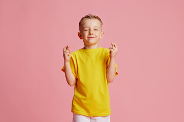 Good luck at exam. Cute child, boy crossed fingers and closed eyes to get lucky against pink studio...