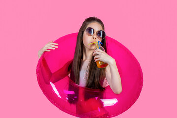 Child girl to swim in sea holding rubber circles. Happy girl in sunglasses holding rubber circle, swimsuit. Kid girl in glasses holds a cocktail, rubber circle for swimming in sea on pink background
