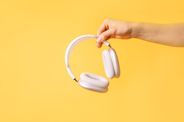 Hand holding white wireless headphones against yellow background.