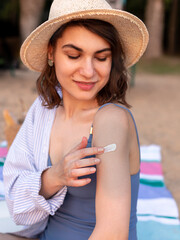 Young woman in straw hat and blue swimsuit applying sun screen cream on her hand on the beach.