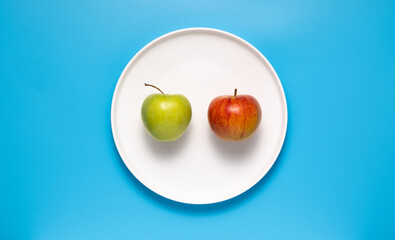 Red and green apple on a white plate on a blue background