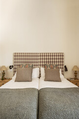 Bedroom with single beds pushed together, wooden bedside tables, fabric upholstered headboards and twin cushions
