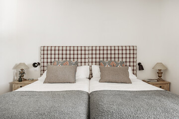 Bedroom with single beds pushed together, wooden nightstands, fabric upholstered headboards,...