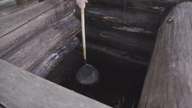Man scoops a bucket up water from a well. Close up.