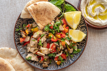 Chicken pieces with vegetables, pita bread, hummus with olive oil for Mediterranean lunch.