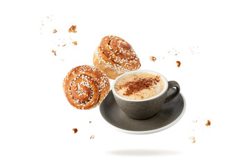 Cup hot cappucino coffee and fresh baked cinnamon buns with crumbs and sugar pieces flying falling ...
