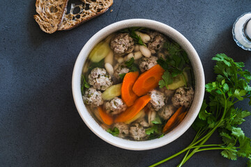 White bean and beef meatball soup with carrots on grey background, directly above