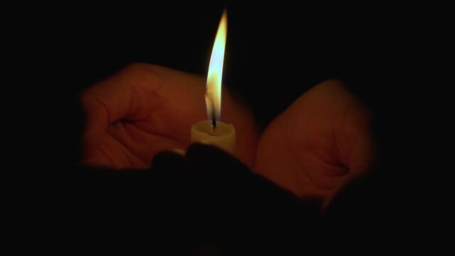Burning wax candle in female hands in the dark. The candle flame illuminates the palms, symbolizing the bitterness of loss, death, and grief. A woman mourns her husband or son who died in the war