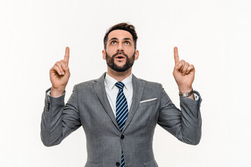 Amazed Caucasian young businessman pointing upwards with fingers isolated over white background. Happy successful manager banker ceo showing sale promotion discount