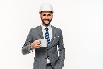 Energetic young engineer in helmet drinking coffee isolated over white background. Happy Caucasian...