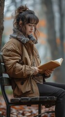 Young girl sitting on a park bench while reading a book.
