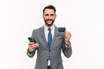 Cheerful young businessman using e-banking with credit card isolated over white background. Rich...
