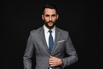 Image of young handsome businessman in formal outfit looking at the side isolated over black background. Attractive successful man manager hr posing in grey tuxedo formal style