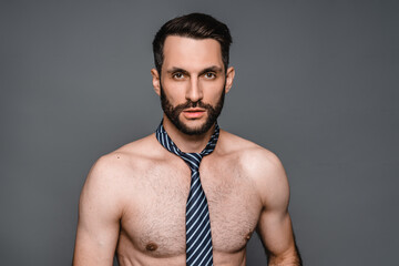 Handsome young naked man wearing tie looking at the camera isolated in grey background. Sexy symbol, womanizer man with muscles and 6 pack portrait. Stripper