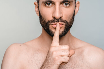 Closeup portrait of young naked man with finger on lips gesture isolated over grey background. Sexy...