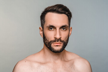 Cropped young naked man with beard and hairstyle looking at the camera isolated over grey background. Sexy handsome guy male model taking care of his appearance