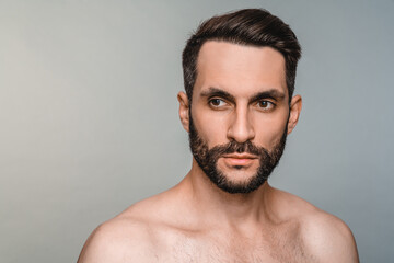 Serious young shirtless man with muscles and beard isolated over grey background. Caucasian sexy...