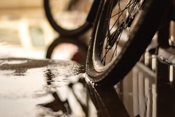 Rear bicycle wheel which is flat and parked on wet floor of house garage, soft focus.