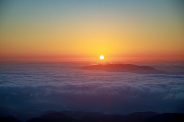 Beautiful sunrise at dawn over a sea of ​​clouds and mountains towering between them