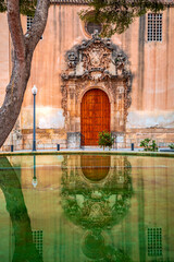 Facade of the Carmen church with its entrance reflected in a fountain, in Orihuela, Alicante, Valencian Community, Spain