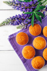 Freshly baked muffins and purple lupins on white wooden background. Homemade baking, preparing sweet dessert. Summer recipe. Vertical photo.