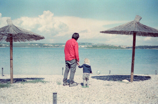 Father and Child Enjoying Seaside Under Thatched Umbrellas