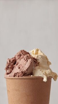 Close up of roating vanilla and chocolate flavor ice cream in brown paper take away cup. Summer dessert. Light grey color background
