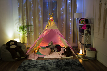 Charming home bedroom transformed into a magical night campsite for a little girl, with fairy lights and plush toys