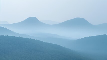 Naklejka premium A view of a mountain range shrouded in fog, with distant mountains and trees in the foreground