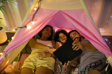 Joyful family savors a cozy, intimate evening in a homemade tent illuminated by twinkling fairy lights