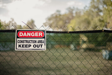 Danger Construction area sign hanging on a chain link fence at a construction site,  horizontal, side space